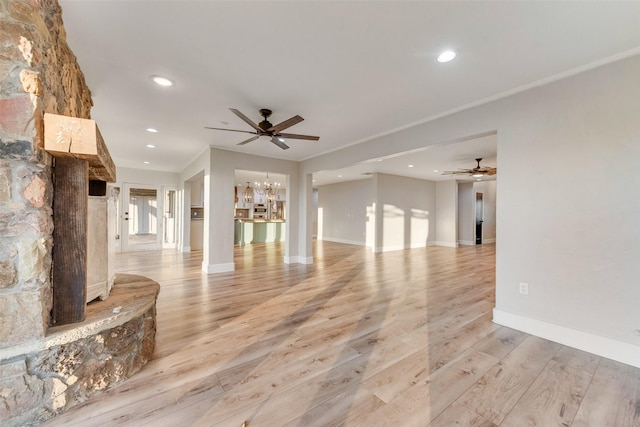 unfurnished living room featuring crown molding, ceiling fan with notable chandelier, and light wood-type flooring