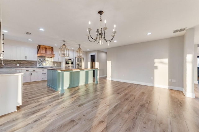 kitchen featuring custom exhaust hood, white cabinetry, a center island, appliances with stainless steel finishes, and pendant lighting