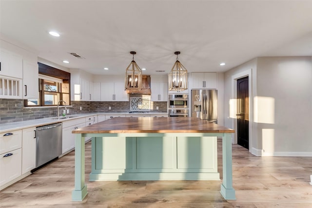 kitchen with a kitchen island, appliances with stainless steel finishes, decorative light fixtures, white cabinetry, and butcher block counters