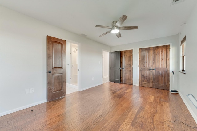 unfurnished bedroom featuring multiple closets, ceiling fan, ensuite bathroom, and hardwood / wood-style floors