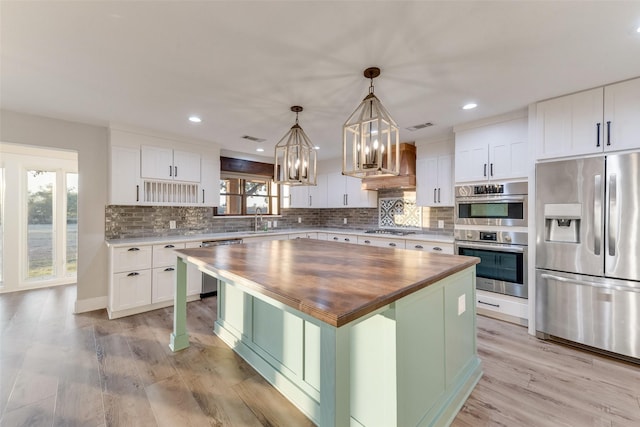 kitchen featuring wooden counters, appliances with stainless steel finishes, a kitchen island, white cabinetry, and hanging light fixtures