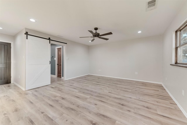 unfurnished room with light hardwood / wood-style floors, a barn door, and ceiling fan