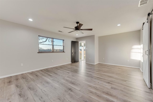 spare room featuring ceiling fan, a barn door, and light wood-type flooring