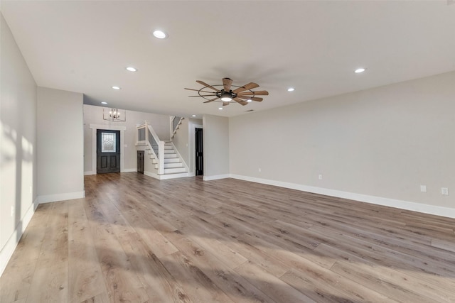 unfurnished living room featuring ceiling fan with notable chandelier and light wood-type flooring