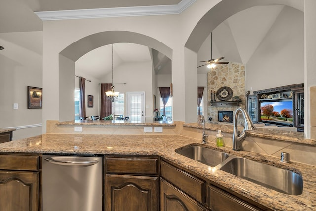 kitchen featuring dark brown cabinetry, sink, a stone fireplace, ceiling fan with notable chandelier, and ornamental molding