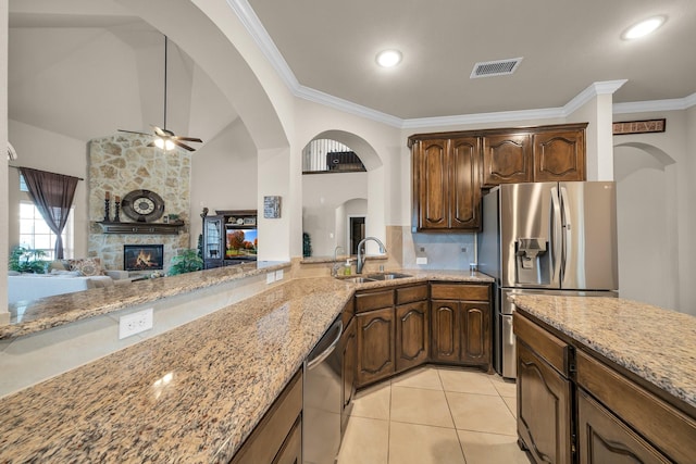 kitchen featuring a stone fireplace, sink, ceiling fan, light stone countertops, and appliances with stainless steel finishes