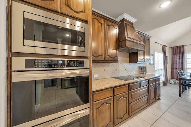 kitchen with stainless steel microwave, lofted ceiling, premium range hood, black electric stovetop, and light tile patterned floors