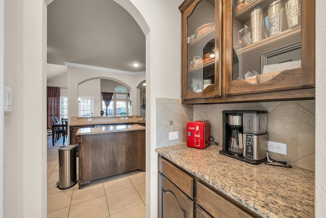 kitchen featuring decorative backsplash, light tile patterned floors, light stone counters, and crown molding