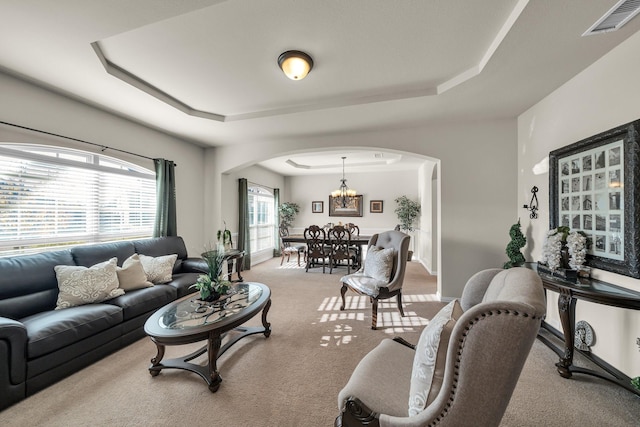 carpeted living room with a raised ceiling and a chandelier