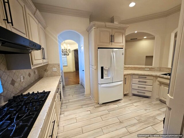 kitchen with black gas cooktop, crown molding, decorative backsplash, white fridge with ice dispenser, and a chandelier