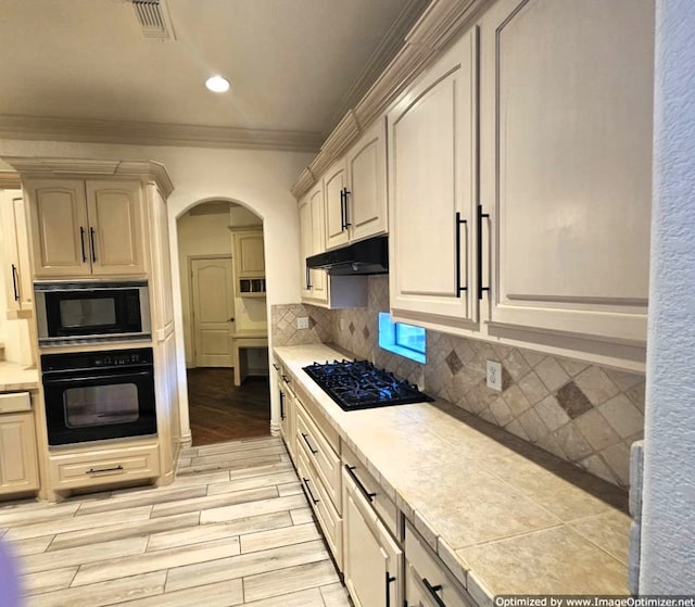 kitchen with tasteful backsplash, crown molding, black appliances, tile countertops, and light hardwood / wood-style floors