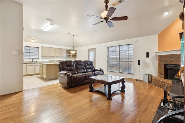 living room featuring ceiling fan, sink, light hardwood / wood-style flooring, vaulted ceiling, and a fireplace