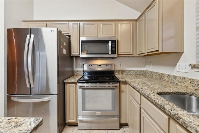 kitchen featuring light brown cabinets, vaulted ceiling, light stone countertops, light tile patterned floors, and appliances with stainless steel finishes