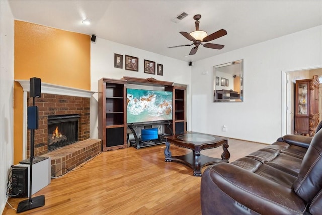 living room featuring hardwood / wood-style floors, ceiling fan, and a brick fireplace