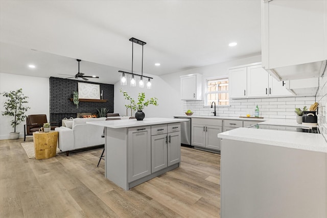 kitchen with a kitchen island, hanging light fixtures, a brick fireplace, stainless steel dishwasher, and a breakfast bar area