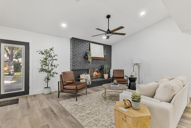 living room with light wood-type flooring, a brick fireplace, and ceiling fan