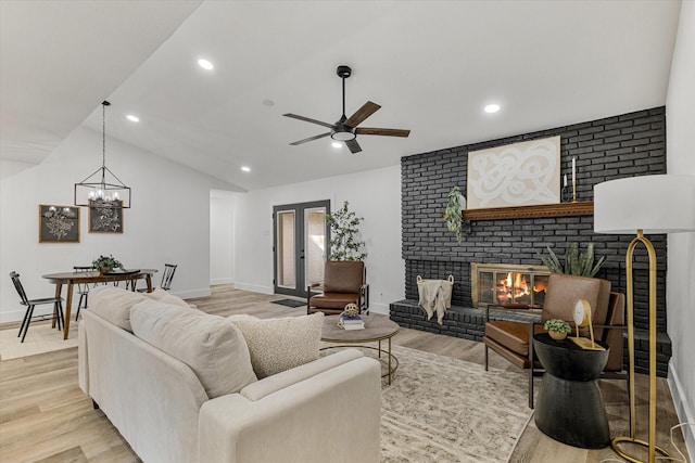 living room featuring lofted ceiling, a fireplace, ceiling fan with notable chandelier, and light hardwood / wood-style floors