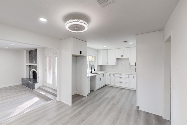 kitchen with white cabinets, a fireplace, sink, and light hardwood / wood-style flooring