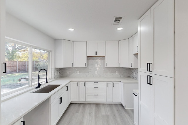 kitchen featuring tasteful backsplash, white cabinetry, sink, and light hardwood / wood-style flooring