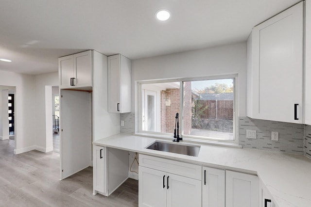 kitchen featuring sink, tasteful backsplash, light stone counters, light hardwood / wood-style floors, and white cabinets