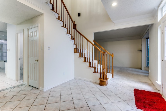 foyer featuring ornamental molding, a high ceiling, a textured ceiling, and light tile patterned floors