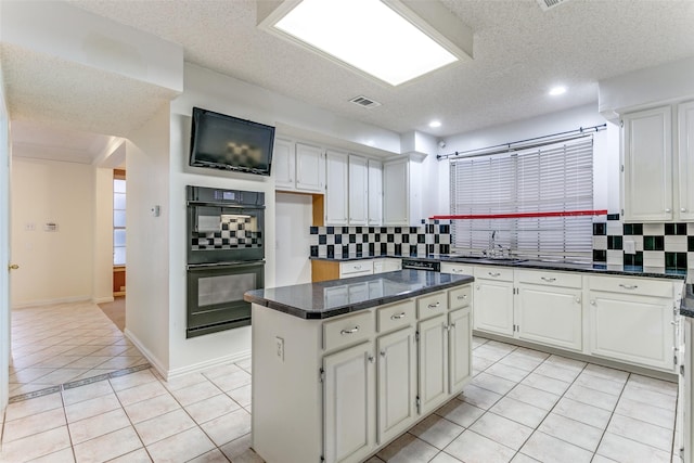 kitchen with sink, light tile patterned floors, black double oven, a center island, and white cabinets