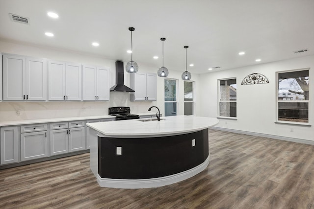 kitchen with wall chimney exhaust hood, black electric range oven, sink, a center island with sink, and pendant lighting