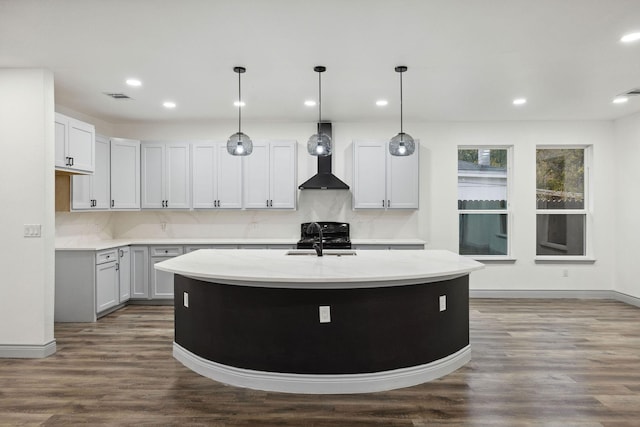 kitchen featuring wall chimney exhaust hood, sink, light stone counters, a center island with sink, and dark hardwood / wood-style floors