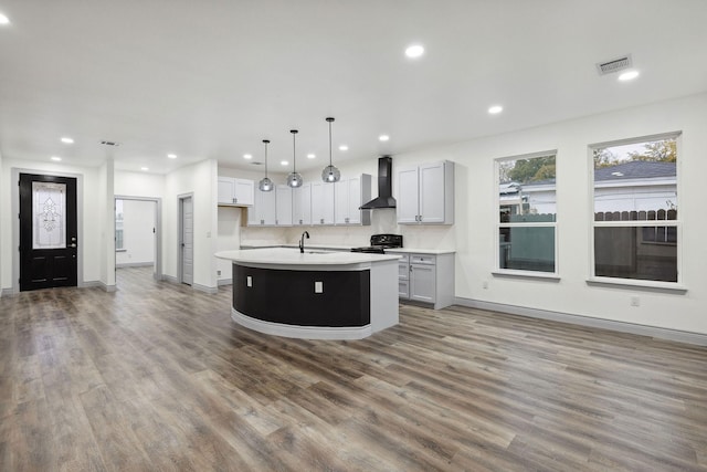 kitchen featuring wall chimney exhaust hood, sink, decorative light fixtures, a center island with sink, and electric range