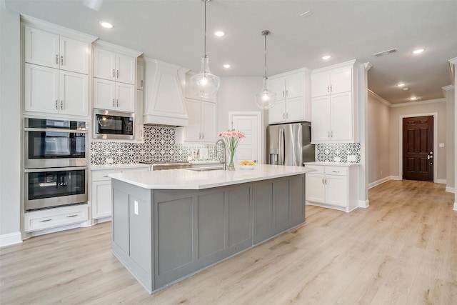 kitchen with white cabinets, appliances with stainless steel finishes, a kitchen island with sink, and sink