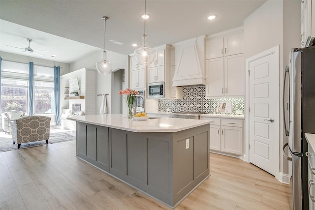 kitchen featuring custom exhaust hood, a center island with sink, hanging light fixtures, white cabinetry, and stainless steel appliances