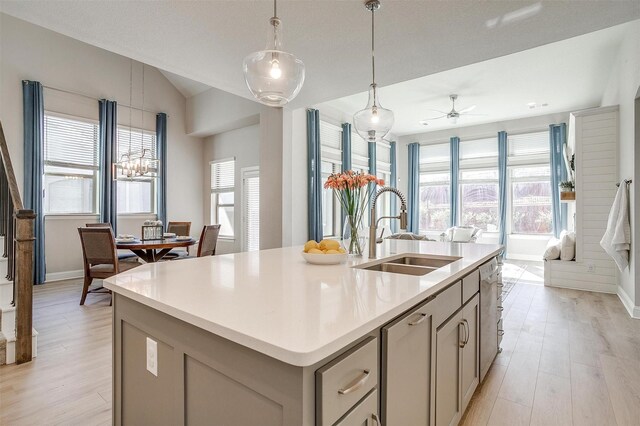 kitchen featuring sink, light hardwood / wood-style flooring, pendant lighting, lofted ceiling, and a kitchen island with sink