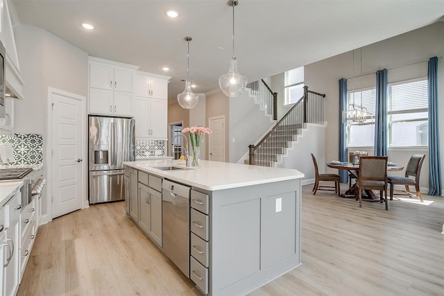 kitchen with sink, an island with sink, light hardwood / wood-style floors, decorative backsplash, and appliances with stainless steel finishes