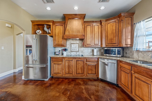 kitchen featuring premium range hood, sink, decorative backsplash, appliances with stainless steel finishes, and light stone counters