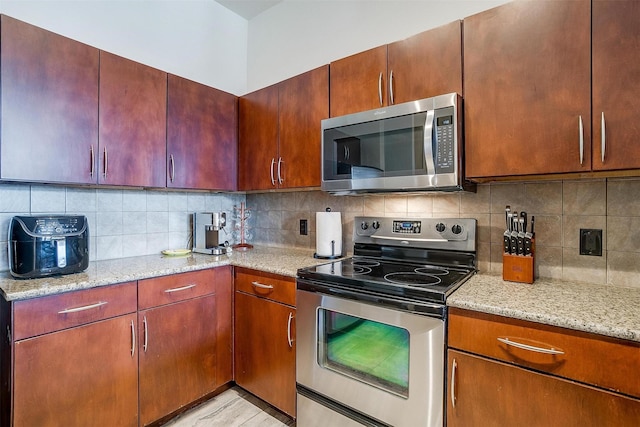 kitchen with light stone countertops, decorative backsplash, stainless steel appliances, and light hardwood / wood-style flooring