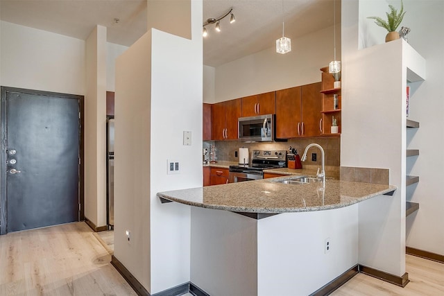 kitchen featuring sink, light hardwood / wood-style flooring, kitchen peninsula, decorative light fixtures, and appliances with stainless steel finishes