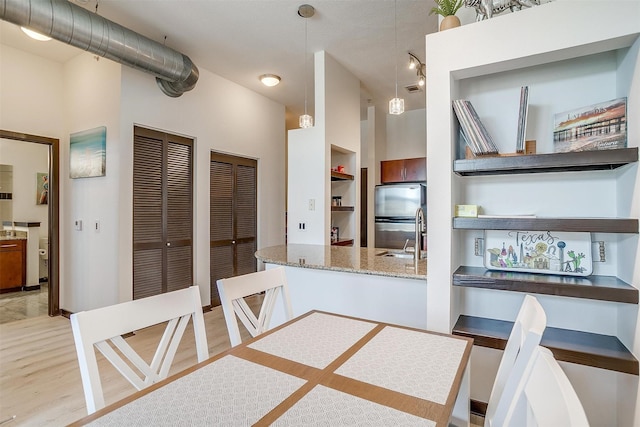 kitchen with pendant lighting, sink, light stone countertops, light hardwood / wood-style floors, and stainless steel refrigerator