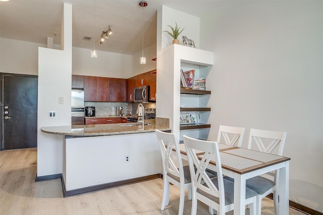 kitchen with pendant lighting, light hardwood / wood-style flooring, dark stone countertops, kitchen peninsula, and stainless steel appliances