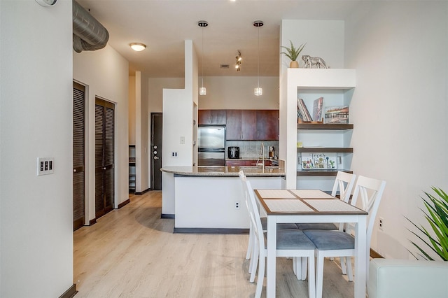 kitchen featuring kitchen peninsula, light hardwood / wood-style flooring, stainless steel fridge, decorative light fixtures, and dark brown cabinetry