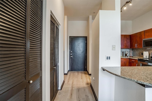 kitchen featuring backsplash, light stone countertops, stainless steel appliances, and light hardwood / wood-style flooring