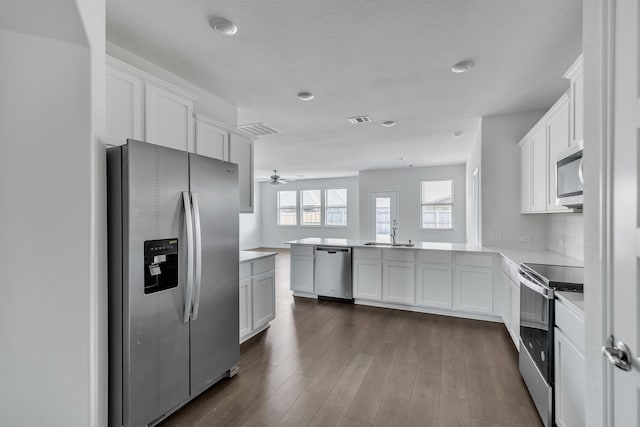 kitchen featuring kitchen peninsula, appliances with stainless steel finishes, ceiling fan, white cabinets, and dark hardwood / wood-style floors