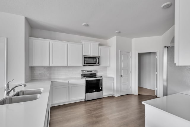 kitchen with appliances with stainless steel finishes, tasteful backsplash, dark wood-type flooring, sink, and white cabinets