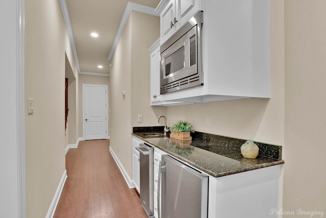 kitchen featuring crown molding, white cabinetry, dark stone countertops, fridge, and stainless steel microwave