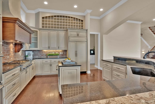 kitchen with sink, stainless steel gas stovetop, hardwood / wood-style flooring, a kitchen island, and ornamental molding