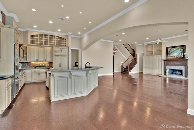 kitchen featuring a brick fireplace, dark stone countertops, cream cabinets, an island with sink, and wood-type flooring