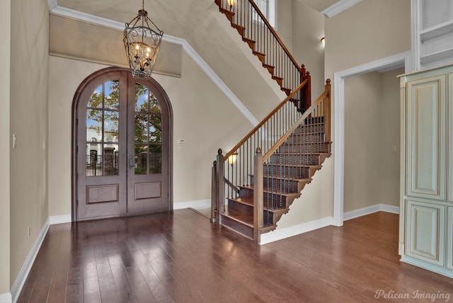 foyer with french doors, dark hardwood / wood-style flooring, crown molding, a towering ceiling, and a chandelier