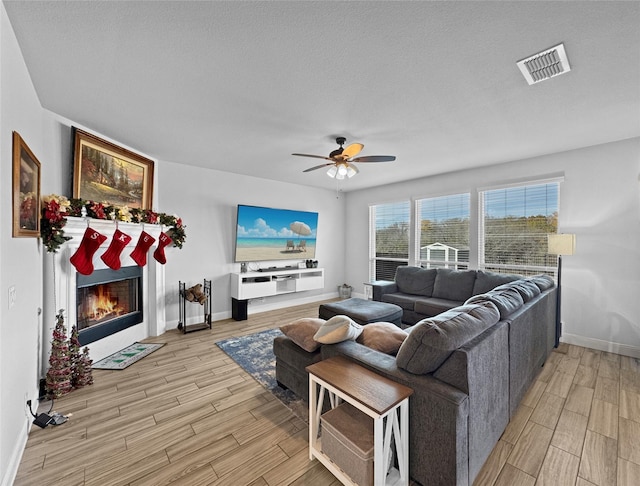 living room featuring ceiling fan, light wood-type flooring, and a textured ceiling