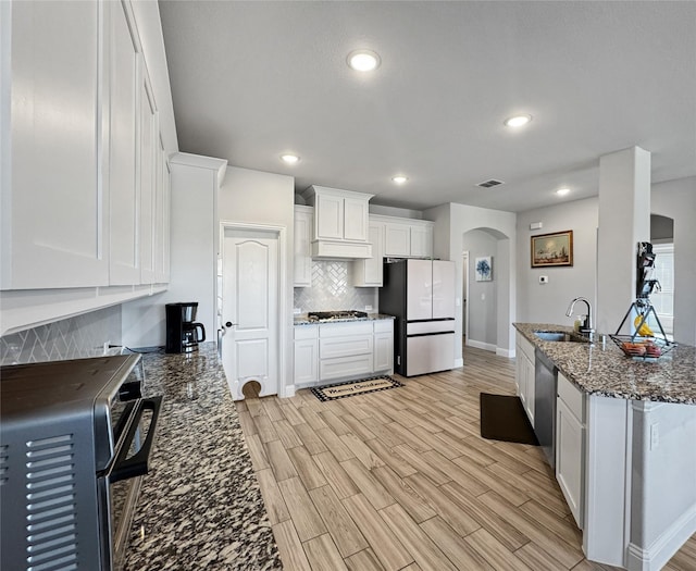 kitchen with dark stone counters, white cabinets, sink, light hardwood / wood-style floors, and stainless steel appliances