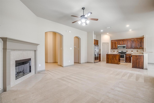 unfurnished living room featuring a tile fireplace, ceiling fan, sink, and light colored carpet