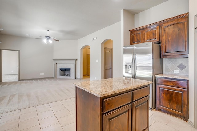 kitchen with light stone countertops, ceiling fan, light carpet, a fireplace, and a kitchen island